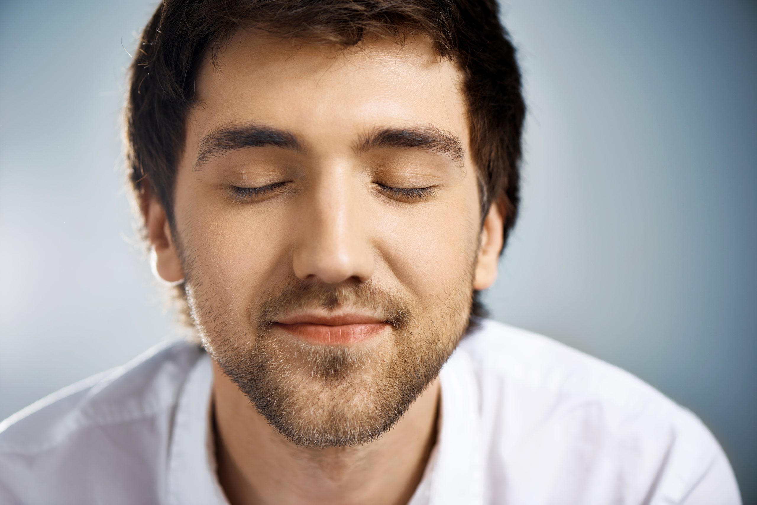 Close up portrait of relaxed elegant handsome young businessman in white shirt with closed eyes. Studio, isolated on grey background.