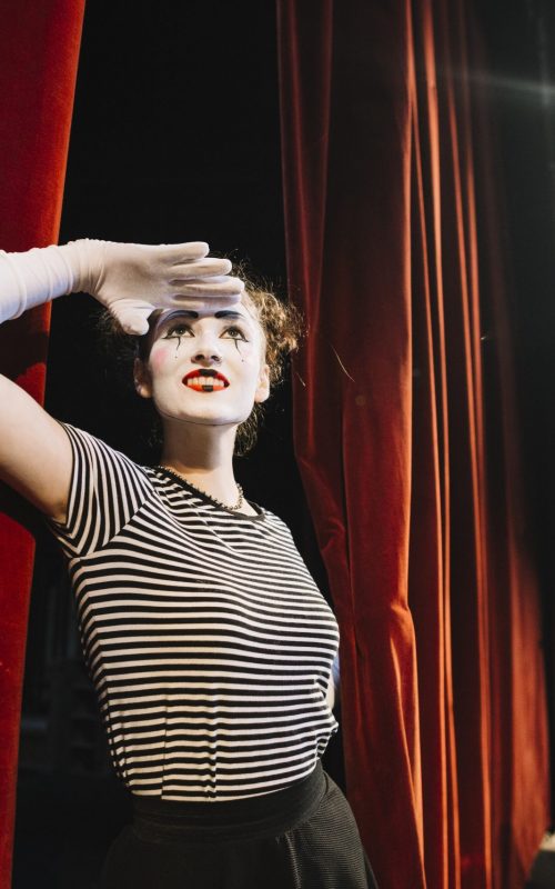 female-mime-artist-standing-near-red-curtain-shielding-her-eyes